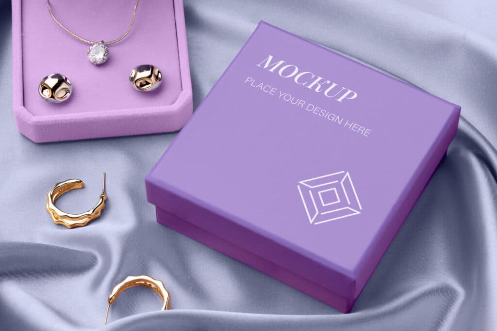 Picture of two purple color custom earring boxes on a purple color surface. There are two gold color earrings on the surface and two platinum color earrings and a necklace inside one of the custom earring boxes,