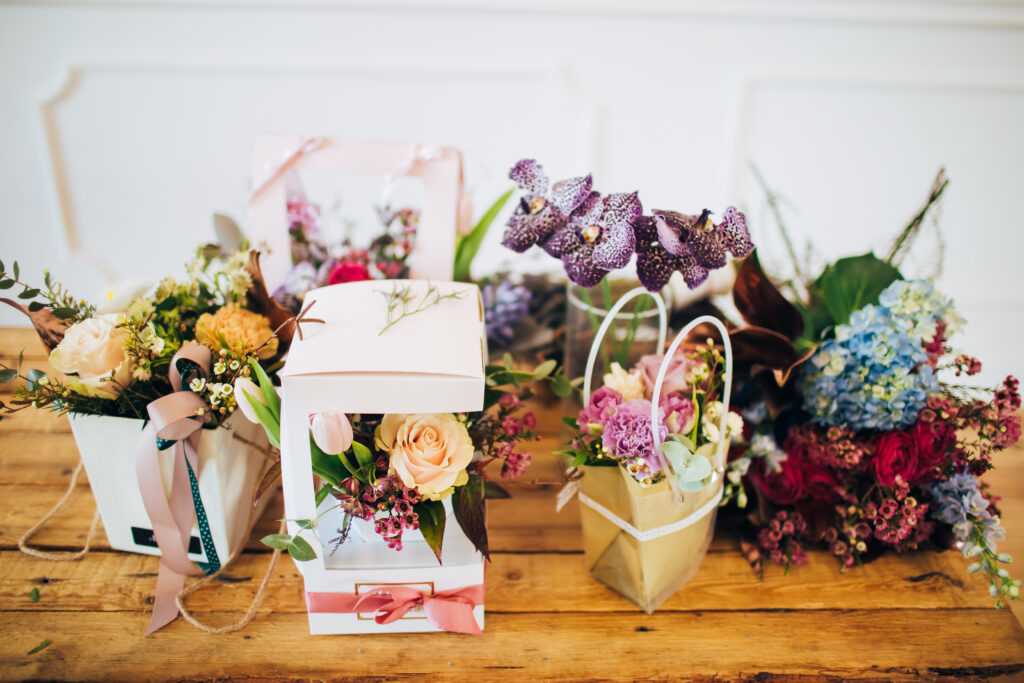 Boxes of flowers stand on a wooden table. 