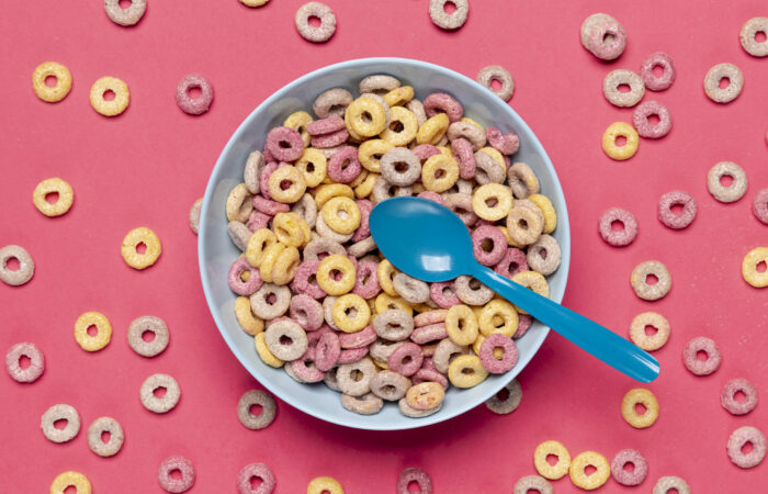 Top view of a bowl of cereal on a pink color surface where cereal spreaded all over
