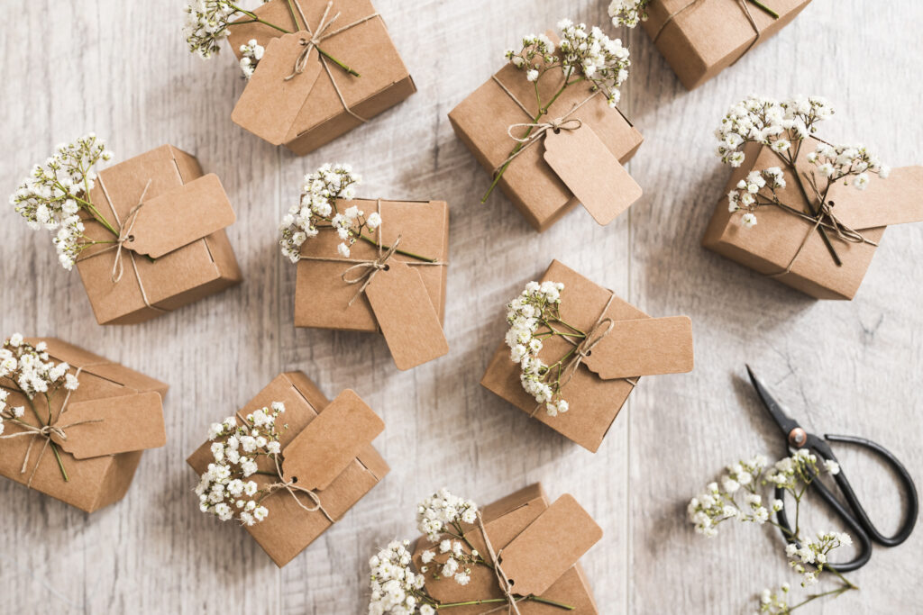 10 cardboard custom favor boxes attached with baby's breath flowers and a black color scissor on a white painted wooden table.