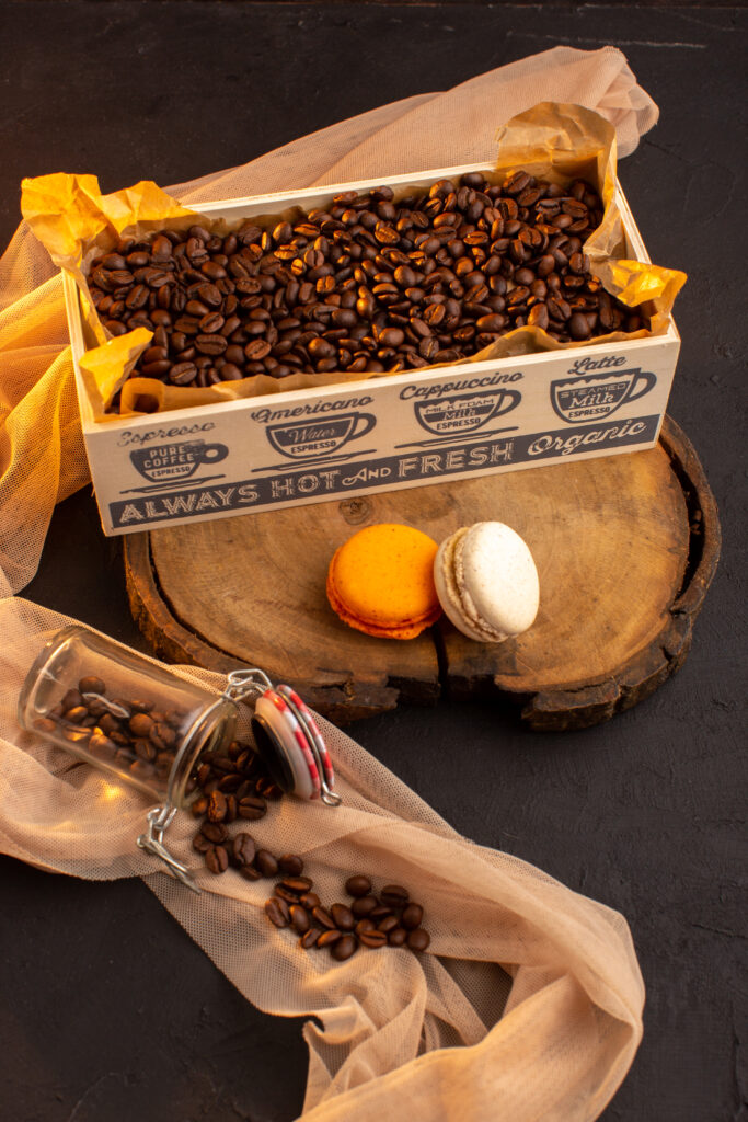 custom subscription box of coffee on top of a wooden tray placed on a black color surface with opened coffee bottle and two macrons in front of it.