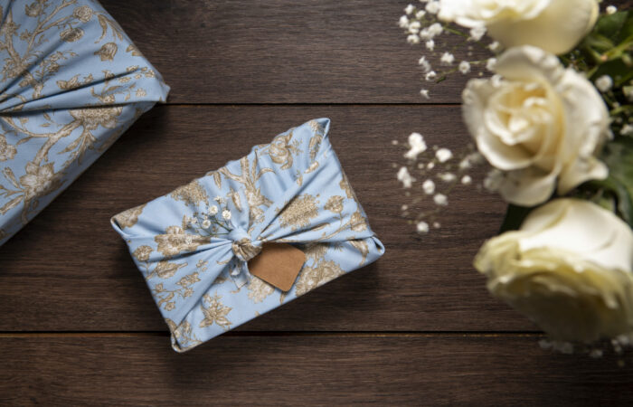 top view of 2 blue color custom favor boxes and half of white rose and baby's breath flower bouquet on a wooden table.