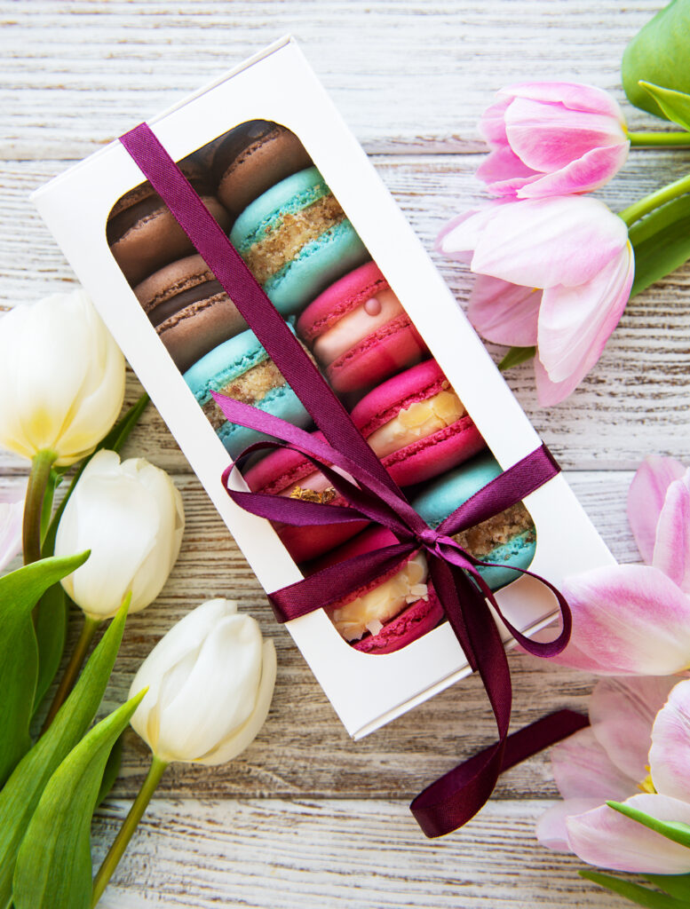 Colorful macaroons in a custom macaron box and tulips on a white wooden  background